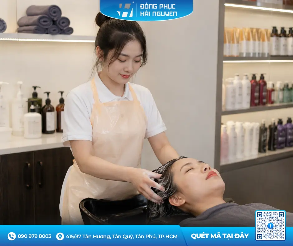 Nhân viên tiệm spa đeo tạp dề chống nước màu kem đang gội đầu và chăm sóc tóc cho khách hàng.