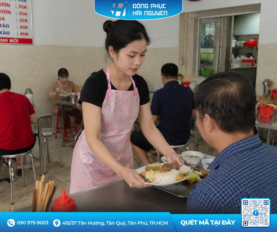 Nhân viên phục vụ quán ăn đeo tạp dề nhựa màu hồng chống thấm nước khi bưng bê món ăn cho khách.