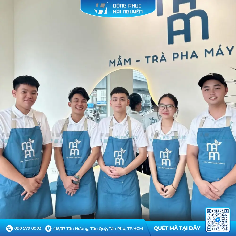 Đội ngũ nhân viên mặc tạp dề quán cafe màu xanh teal in logo thương hiệu chuyên nghiệp
